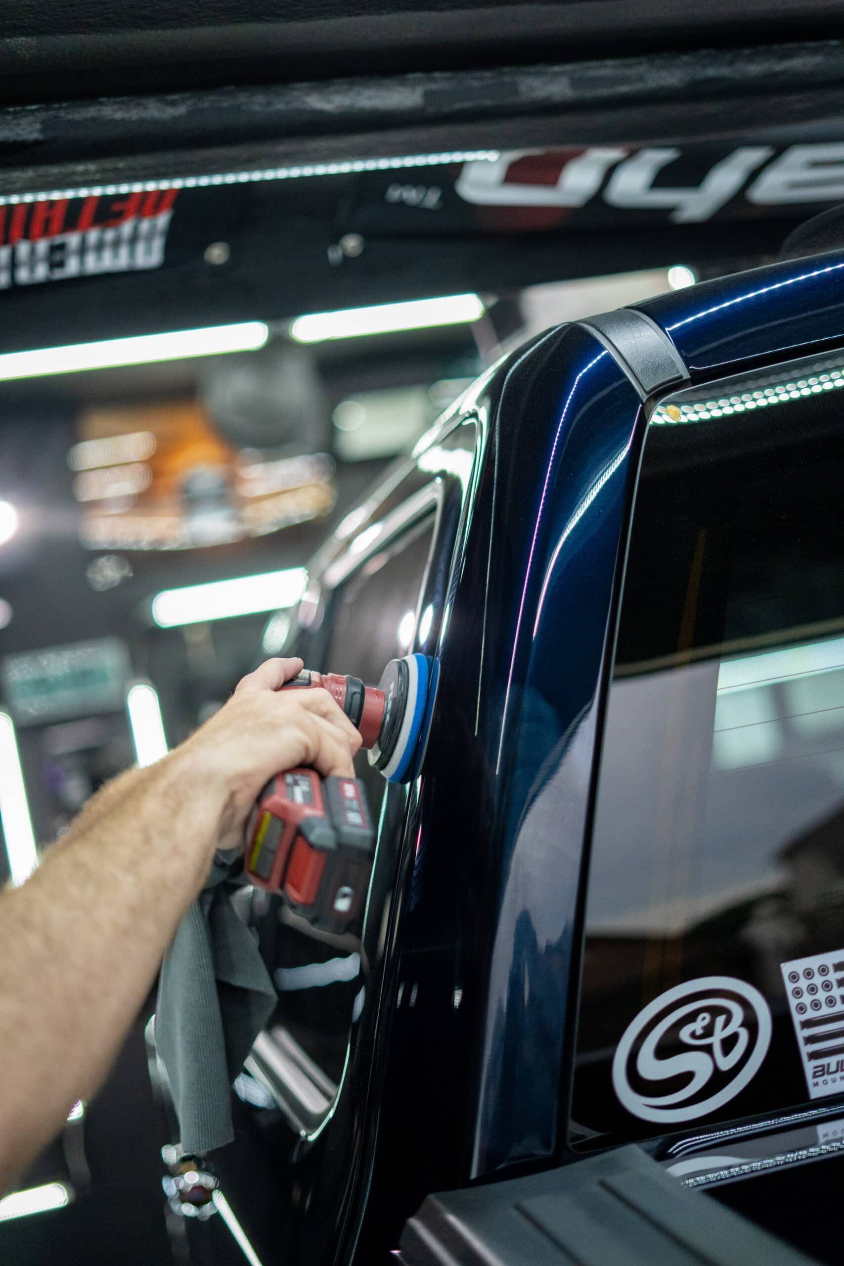 A person is polishing a car with a machine in a garage.