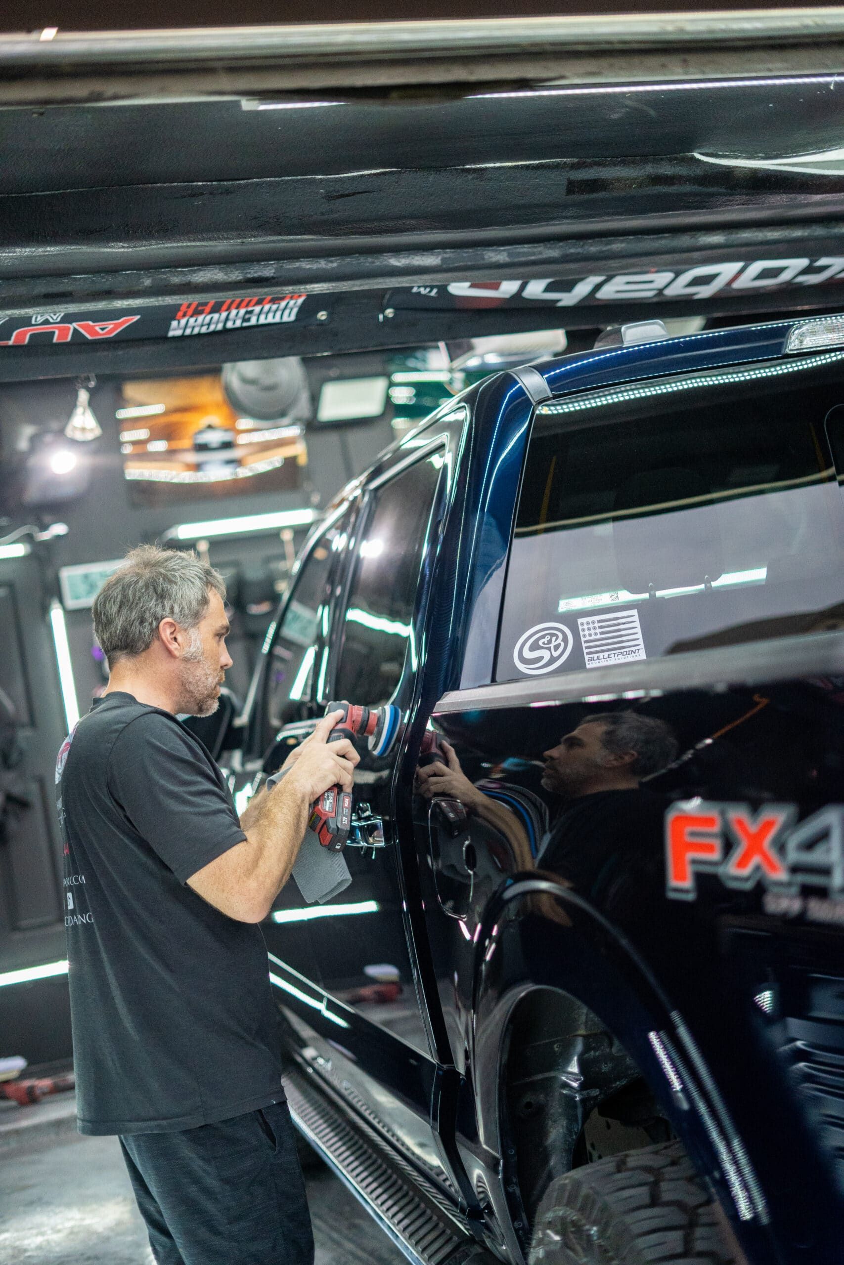 A man is polishing the side of a truck in a garage.