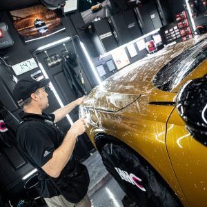 A man is applying a protective film to the hood of a car.