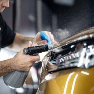 A man is spraying a car headlight with a spray bottle.