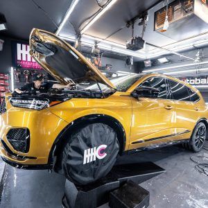 A yellow car with the hood up is sitting on a lift in a garage.