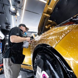 A man is washing a yellow car in a garage.