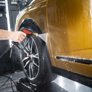 A man is washing a car with a high pressure washer.