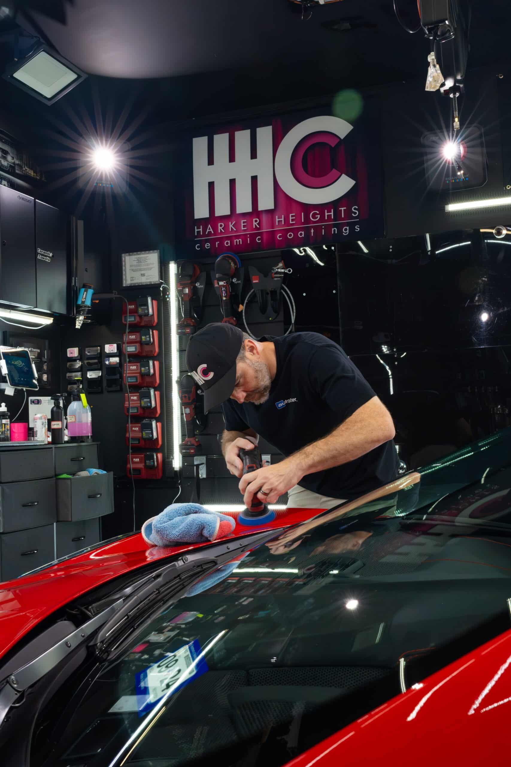 A man is polishing the windshield of a red car in a garage.
