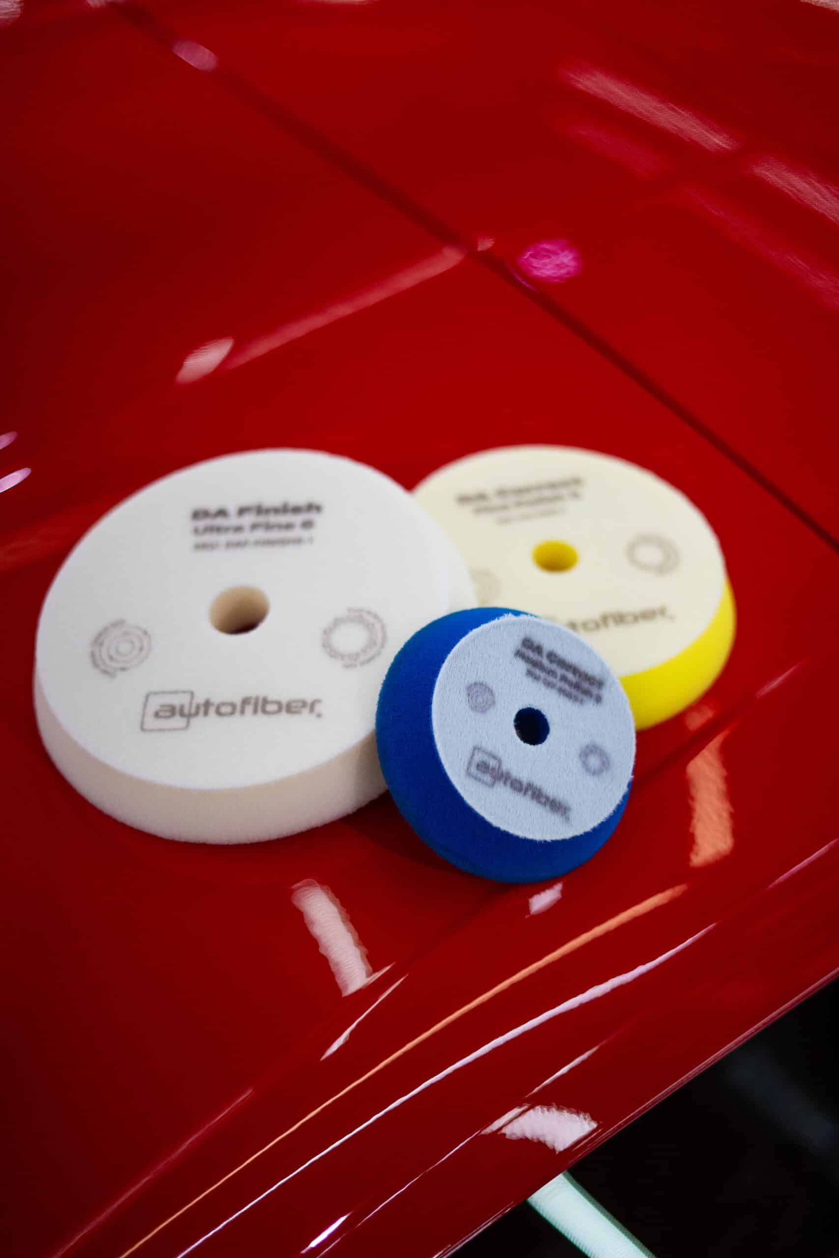 Three polishing pads are sitting on top of a red car