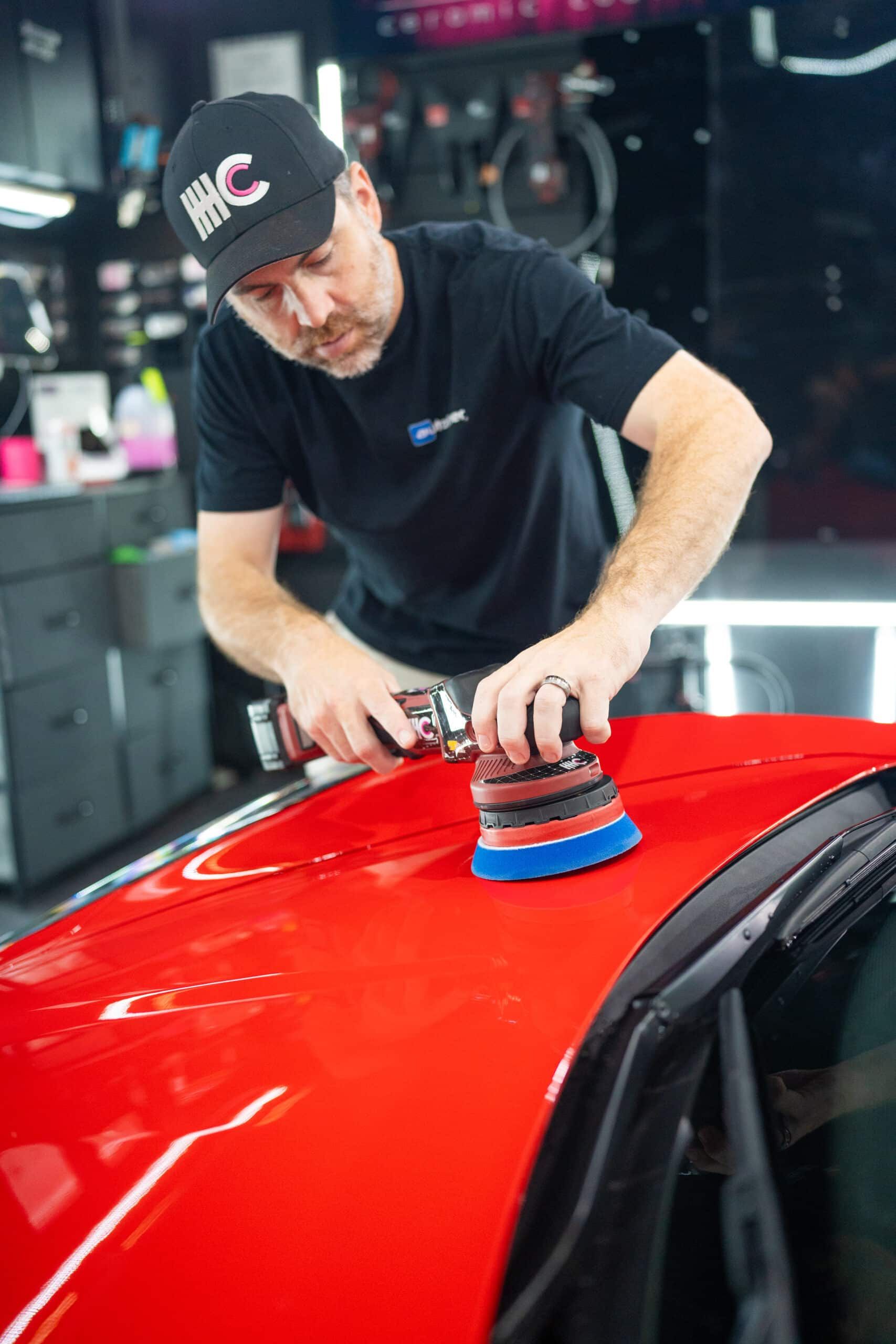 A man is polishing a red car in a garage.