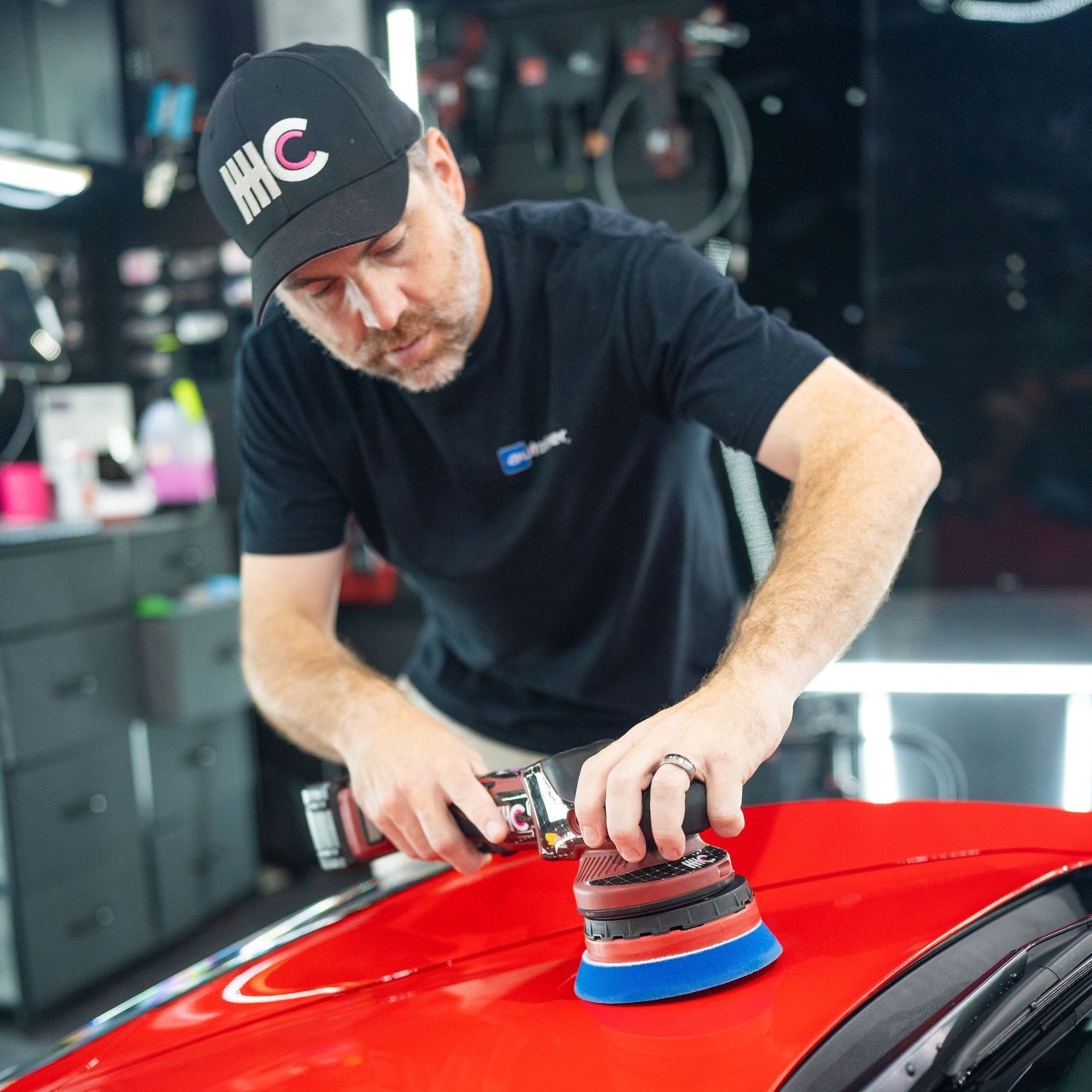 A man is polishing a red car in a garage.