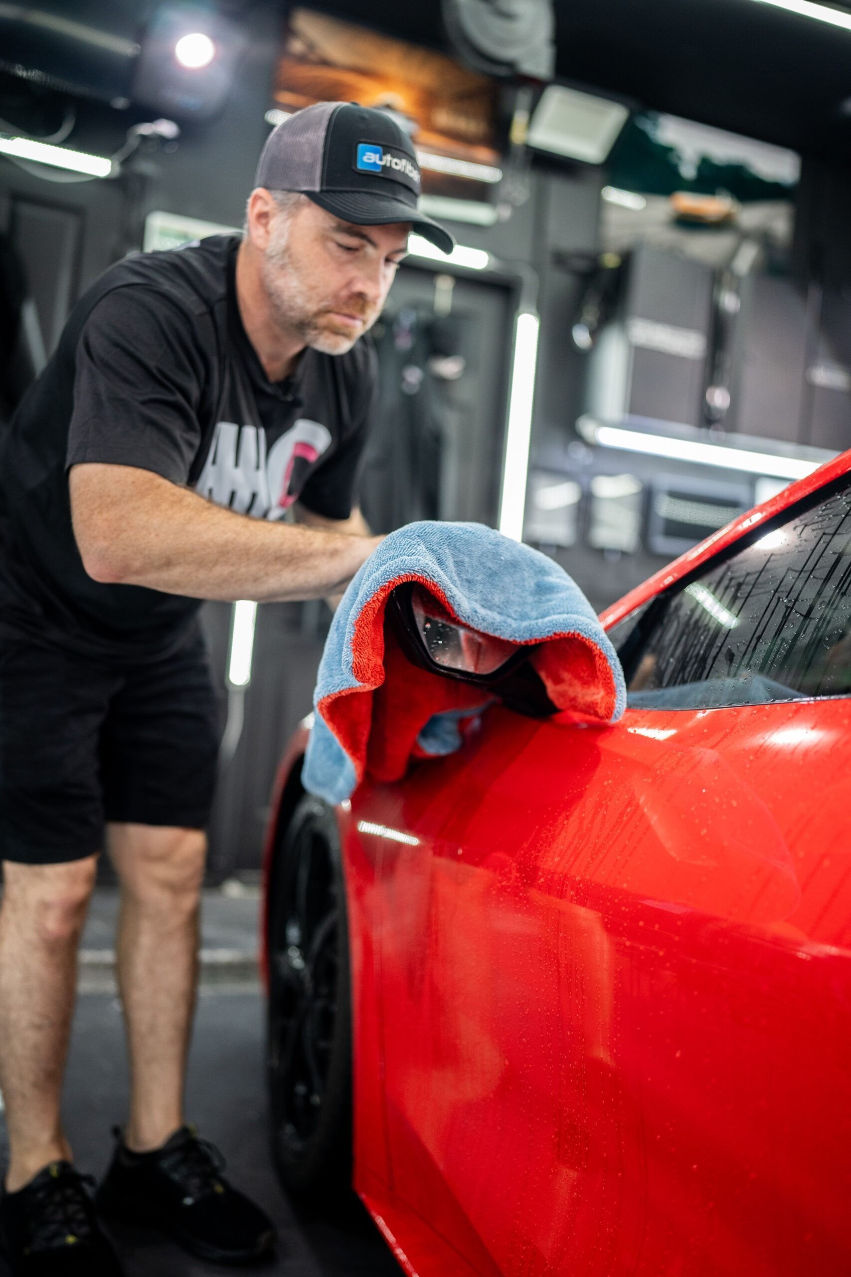 A man is cleaning a red car with a towel.