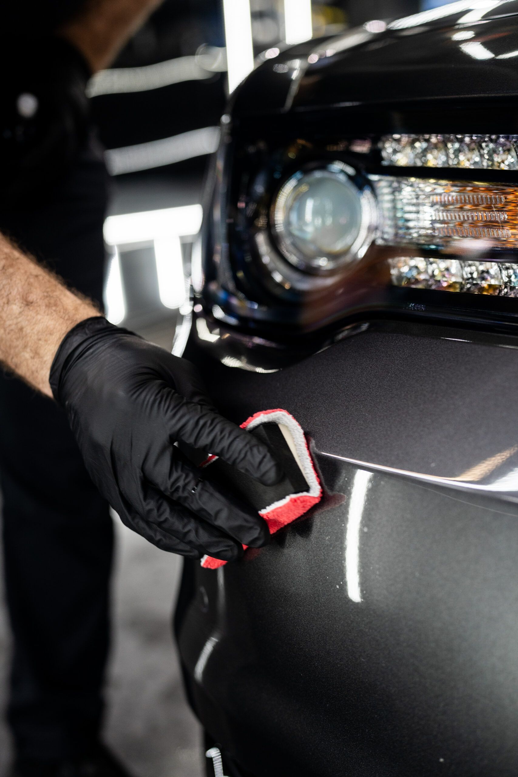A person wearing black gloves is polishing the front of a car.