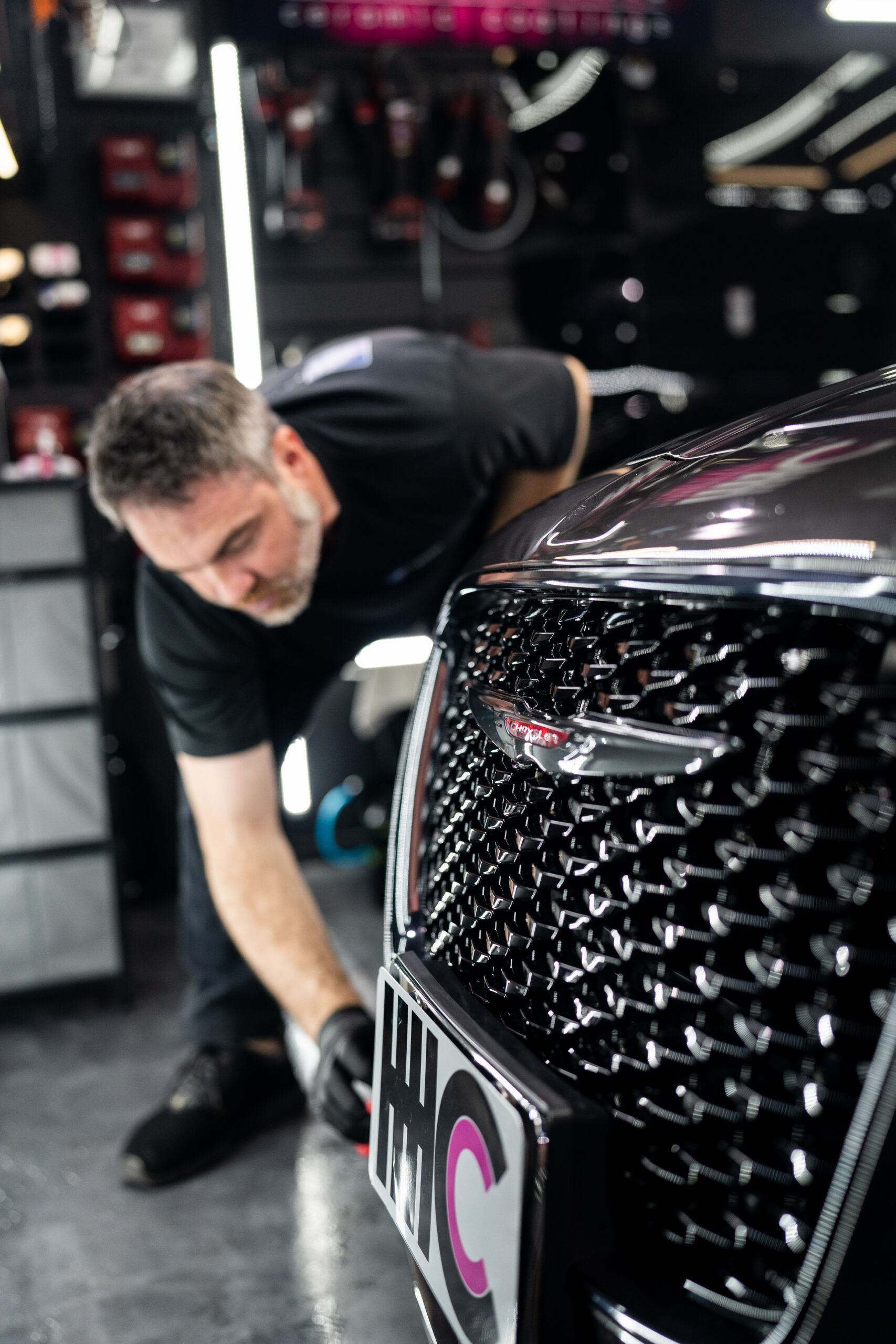 A man is cleaning the front of a black car in a garage.