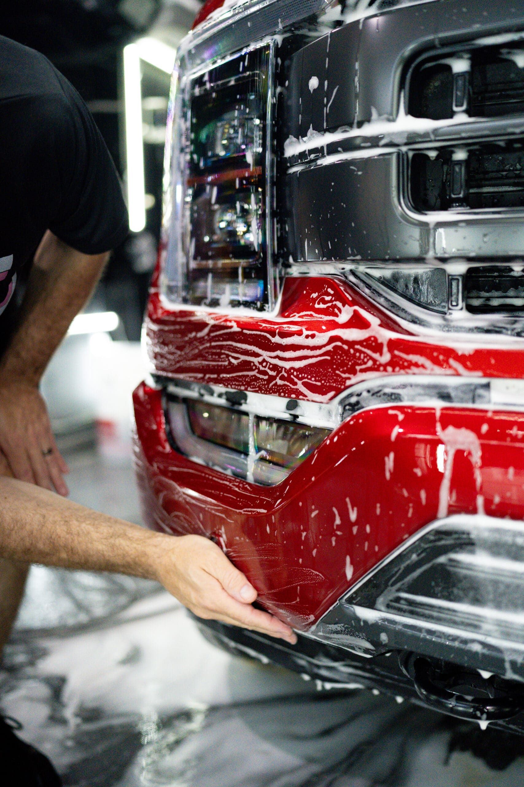 A man is cleaning the front bumper of a red truck.