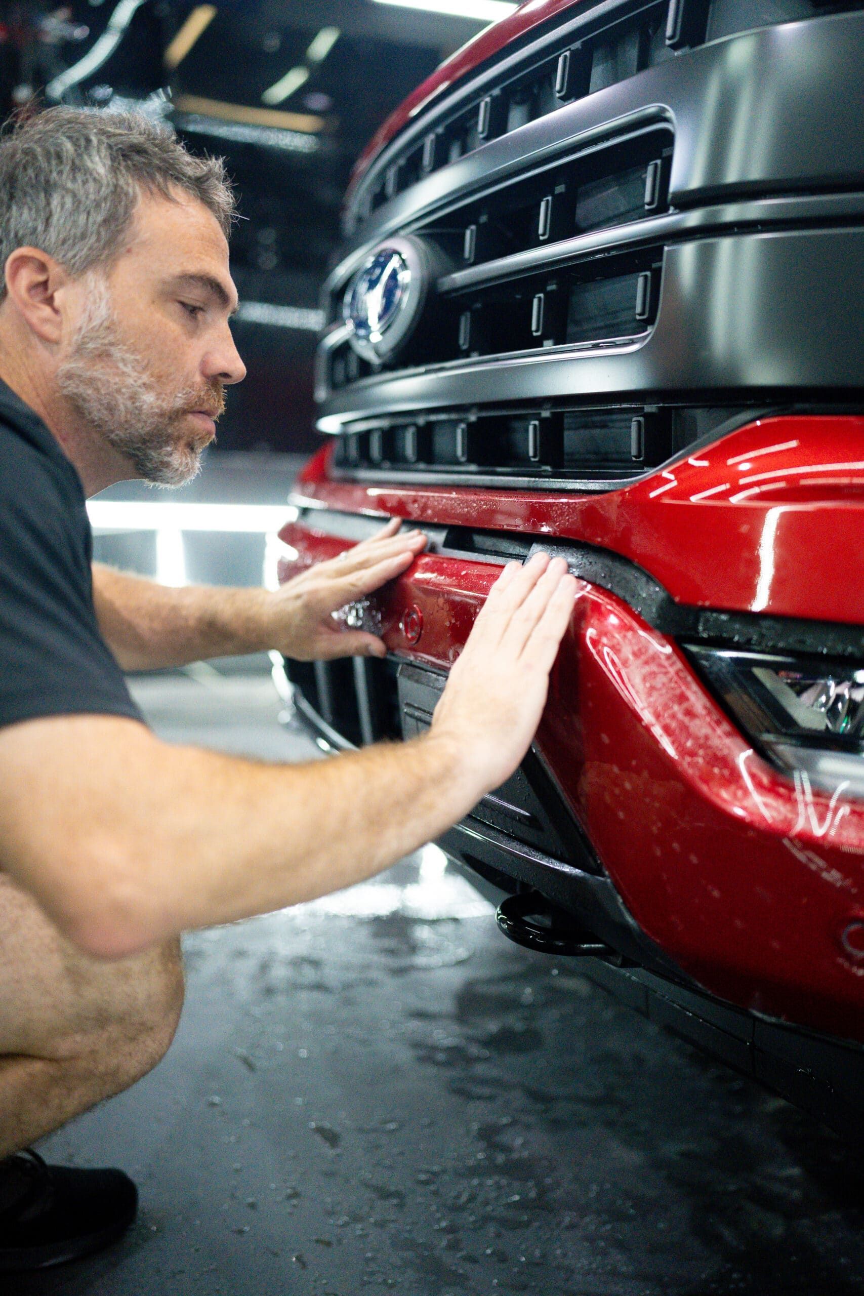 A man is kneeling down and touching the bumper of a red truck.