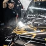 A man is cleaning the hood of a car in a garage.