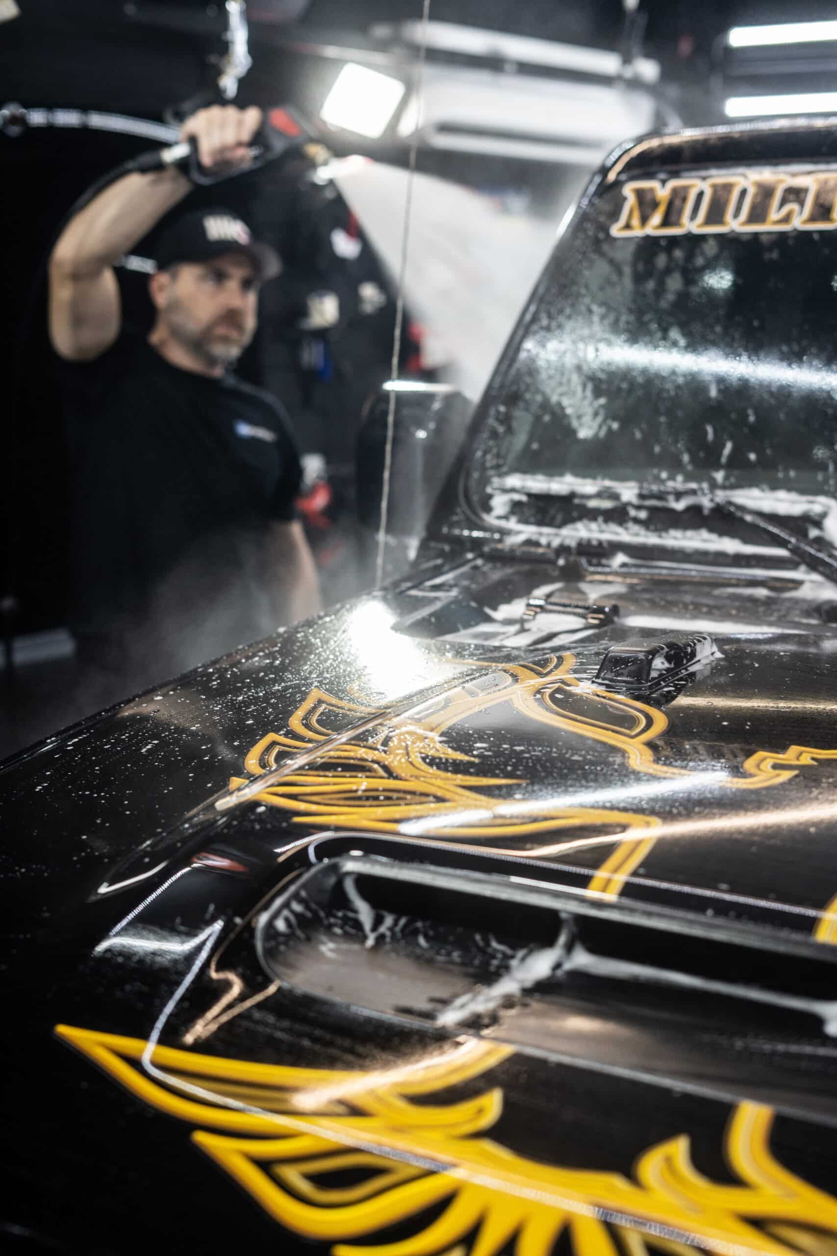 A man is cleaning the hood of a black car with a high pressure washer.