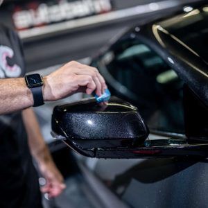 A man wearing an apple watch is cleaning the side mirror of a car.
