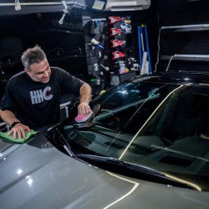 A man is cleaning the windshield of a car in a garage.