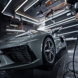 A man is washing a sports car in a garage.