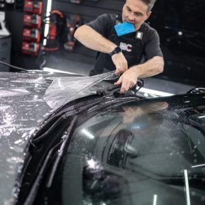A man is applying a protective film to the windshield of a car.