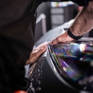 A man is applying a protective film to the headlight of a car.