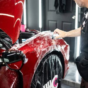 A man is wrapping a red car with plastic wrap.