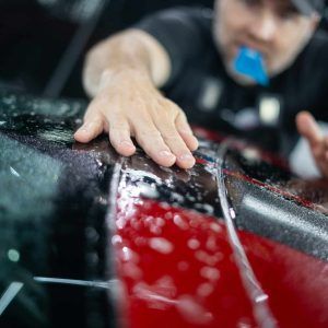 A man is touching a red car with his hand.