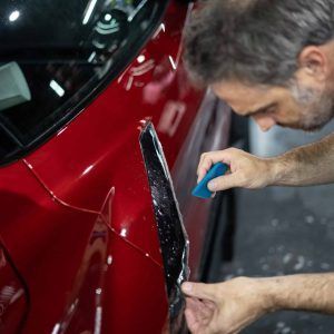 A man is working on a red car with a blue sponge.