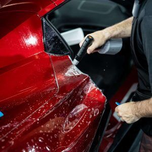 A man is applying a protective film to a red car.