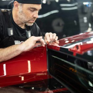 A man is working on a red car in a garage.