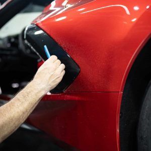 A man is cleaning the side of a red car with a brush.