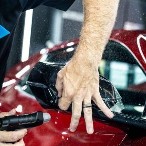 A man is spraying a red car with a hose.