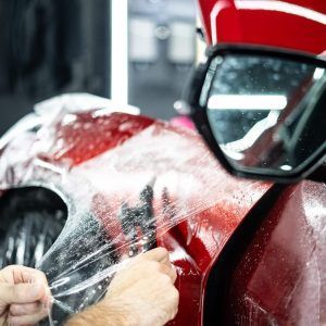 A person is applying a protective film to a red car.