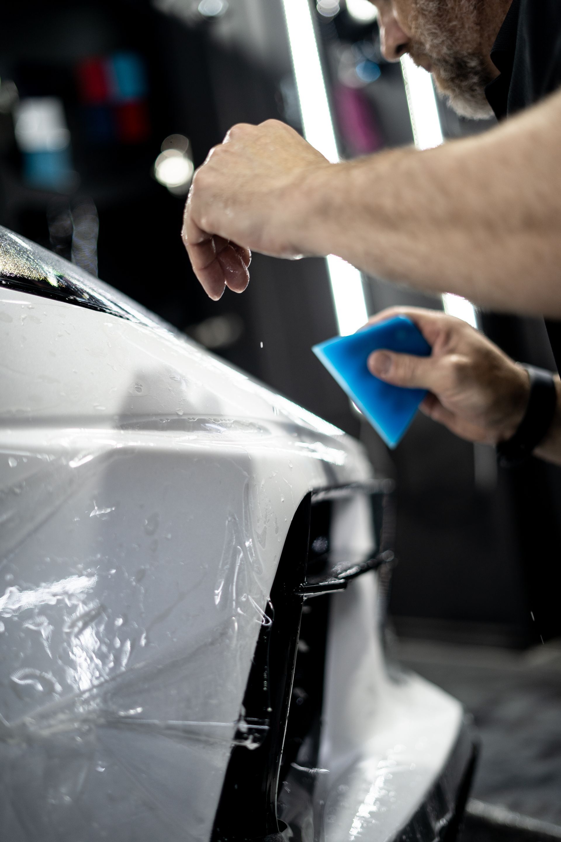 A man is applying a protective film to a white car.