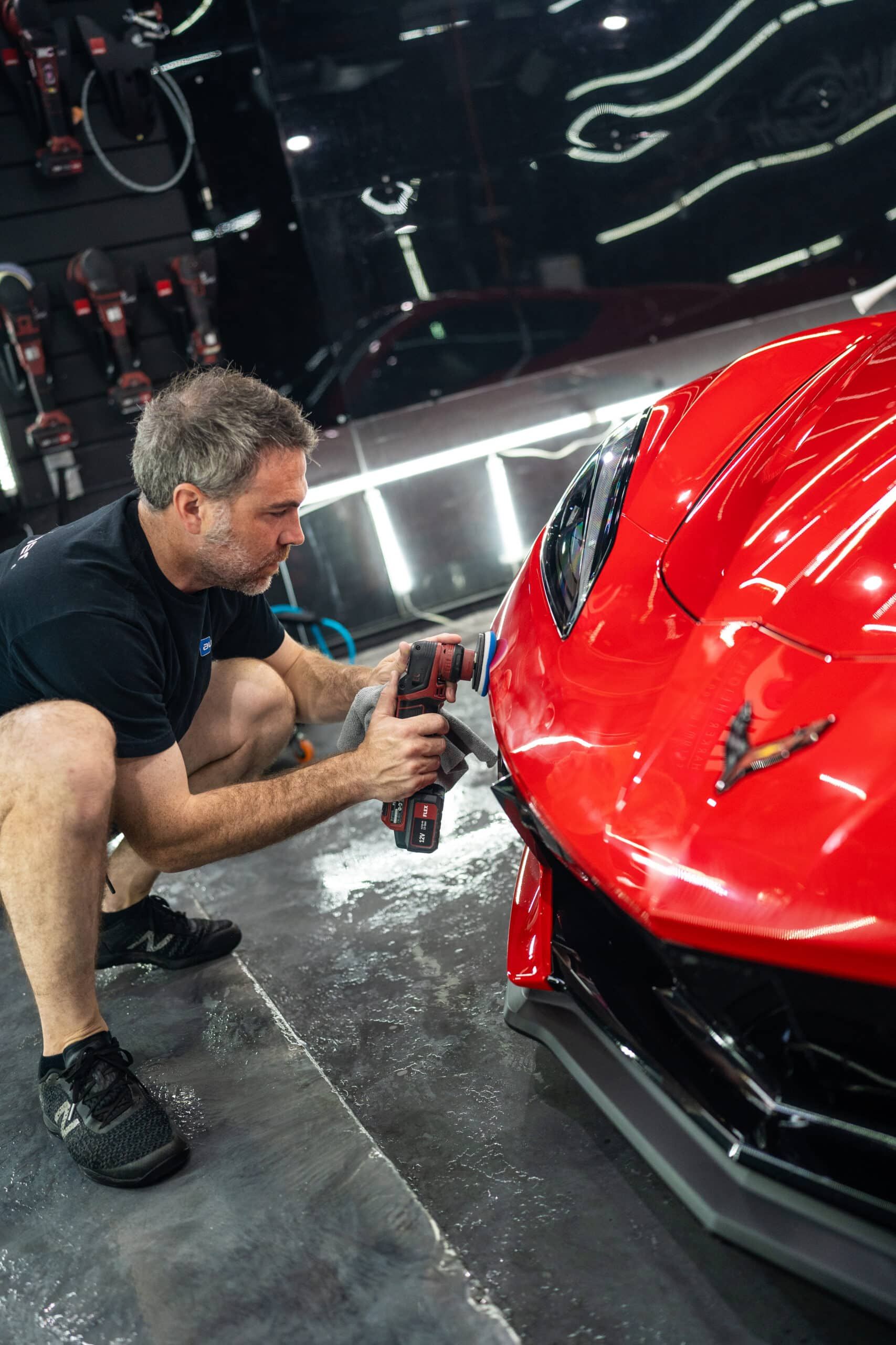 A man is kneeling down next to a red sports car.