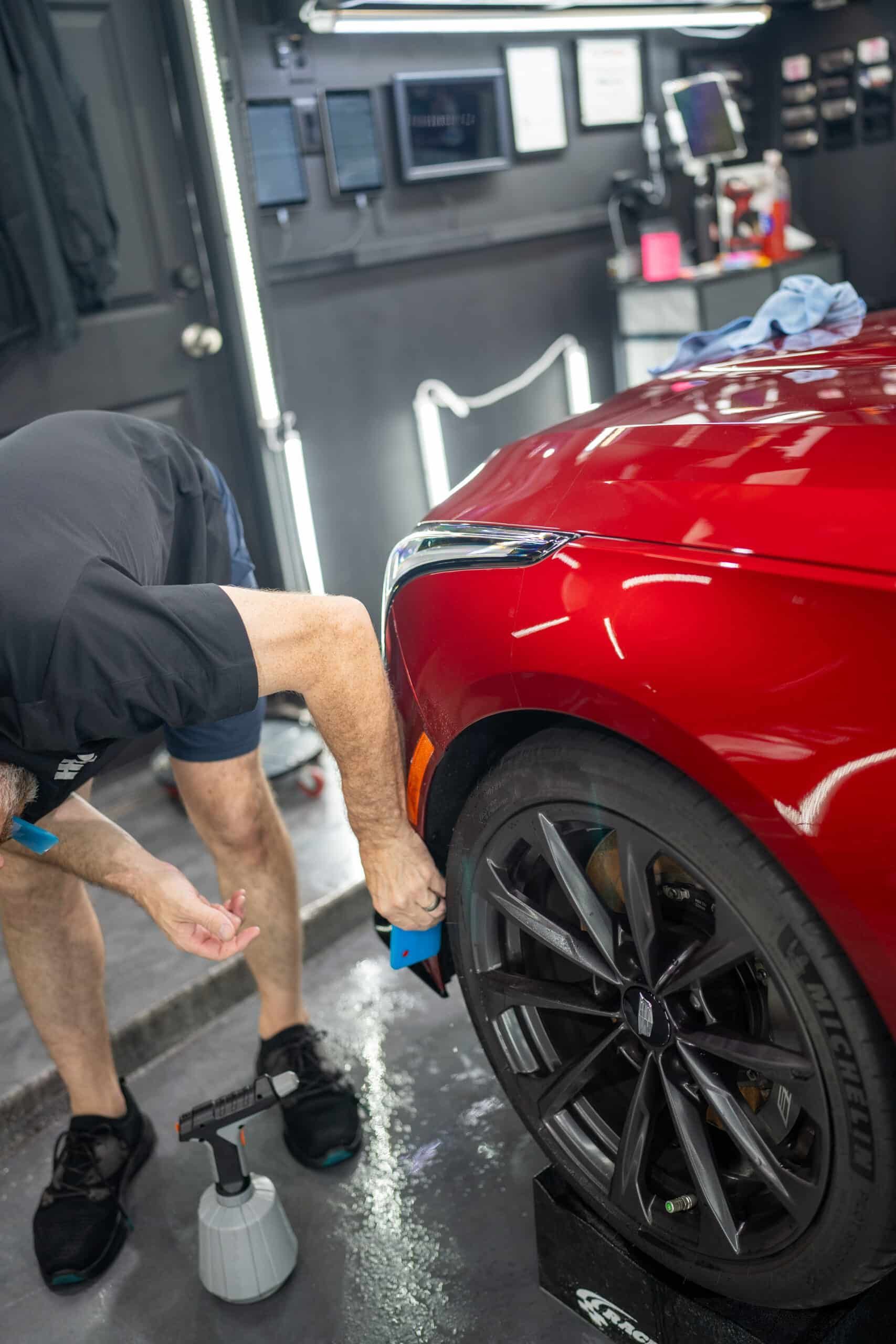 A man is working on a red car in a garage.