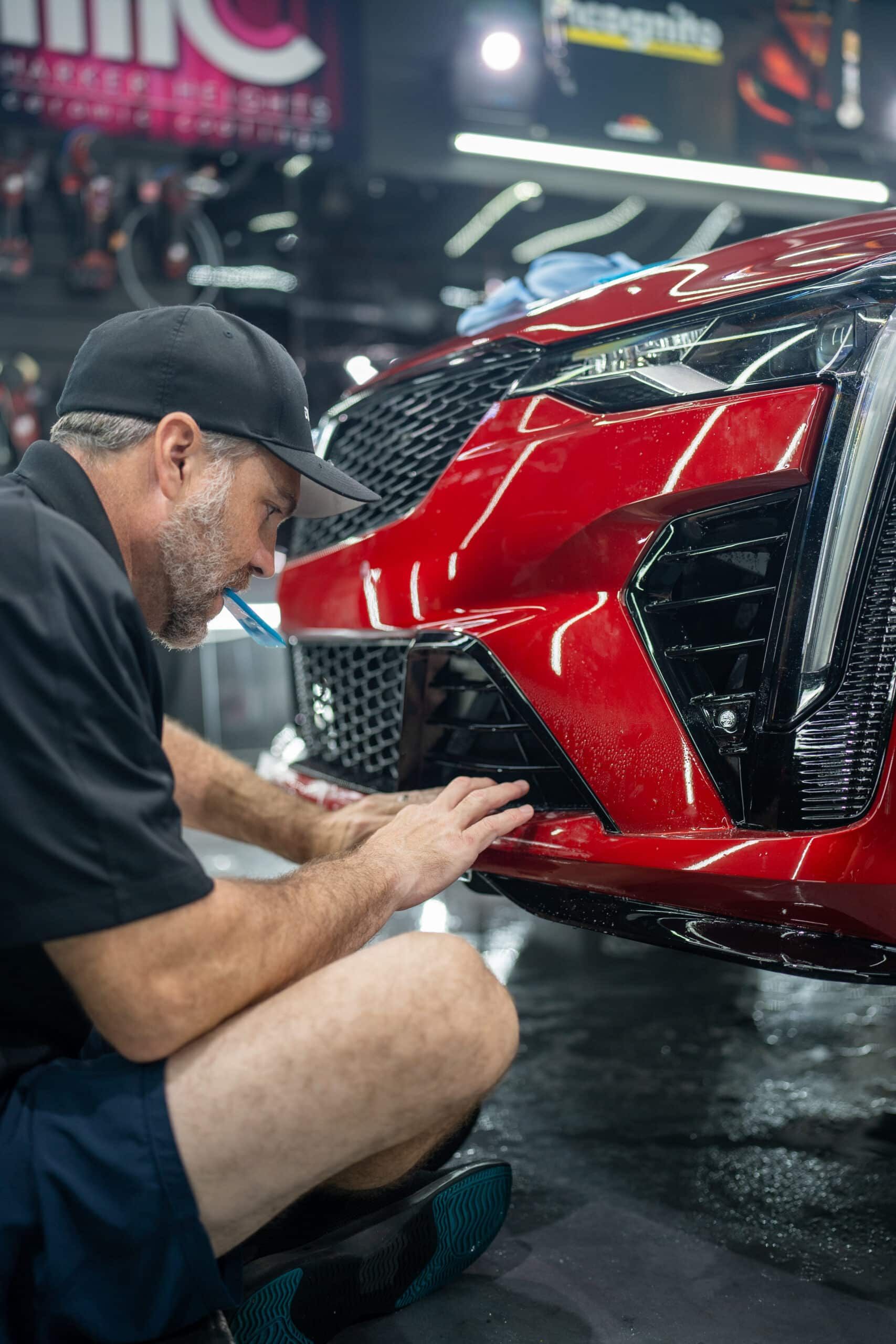 A man is working on the front of a red car.