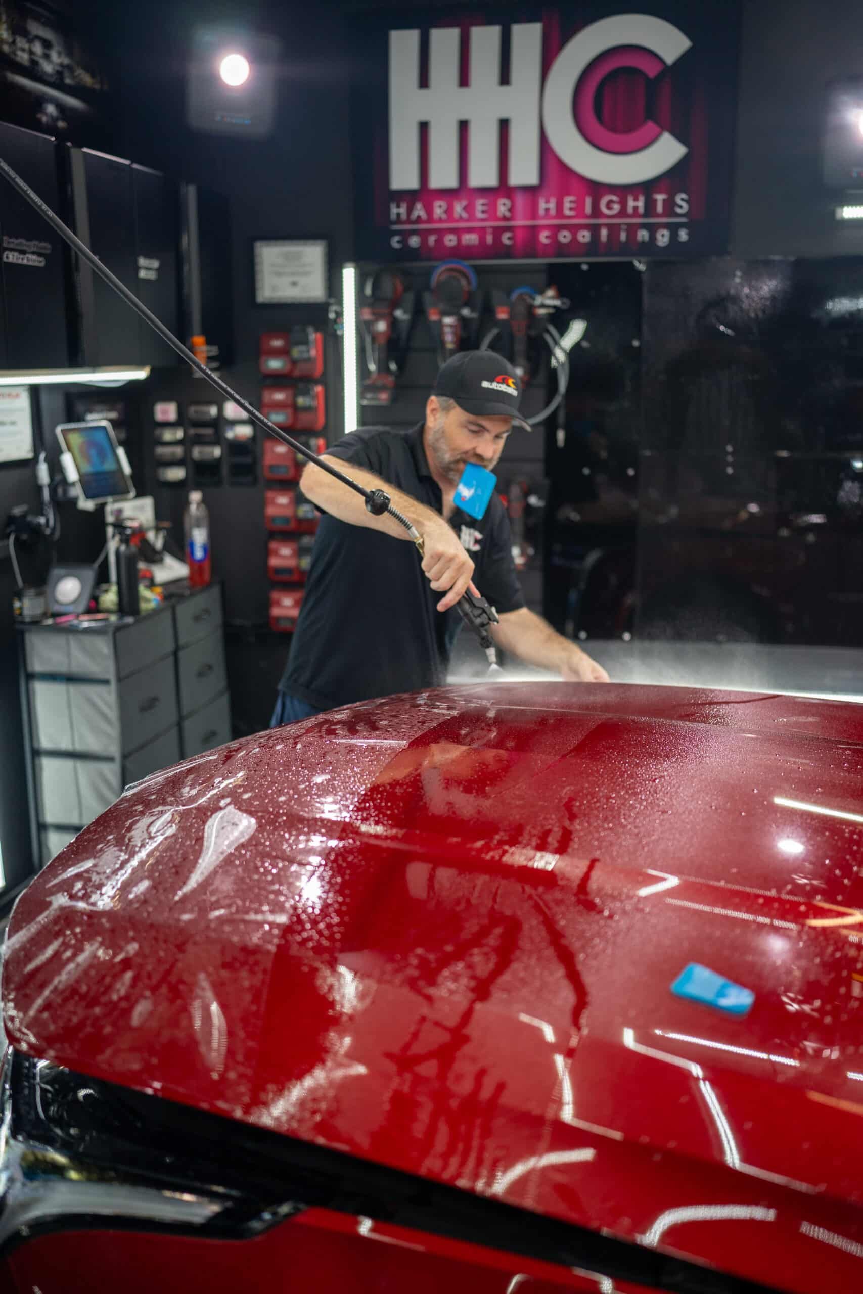 A man is polishing the hood of a red car.