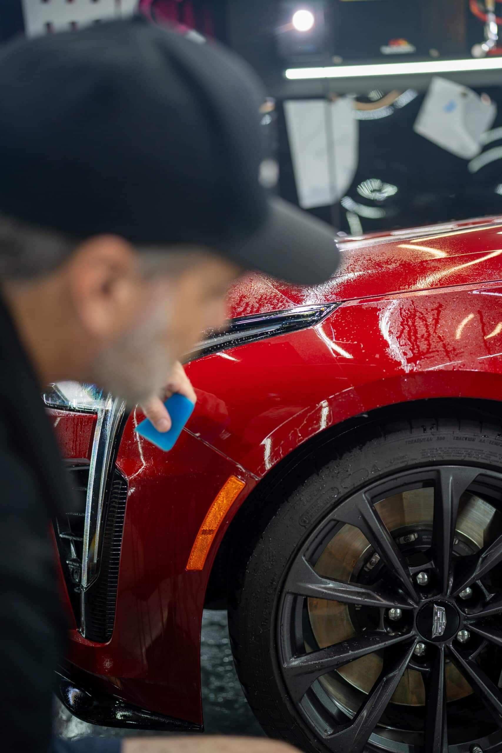 A man is cleaning the fender of a red car with a sponge.