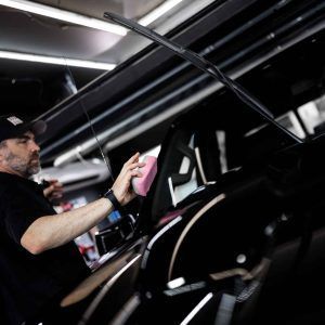 A man is polishing a black car with a pink sponge