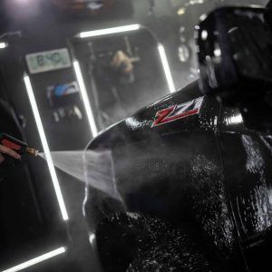 A person is washing a black truck with a high pressure washer.