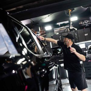 A man is standing next to a black car in a garage.