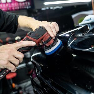 A person is polishing a black car with a machine.