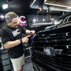 A man is polishing a black car in a garage.