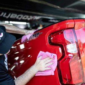 A man is cleaning the back of a red truck with a towel.