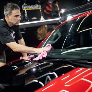 A man is cleaning the windshield of a red car.