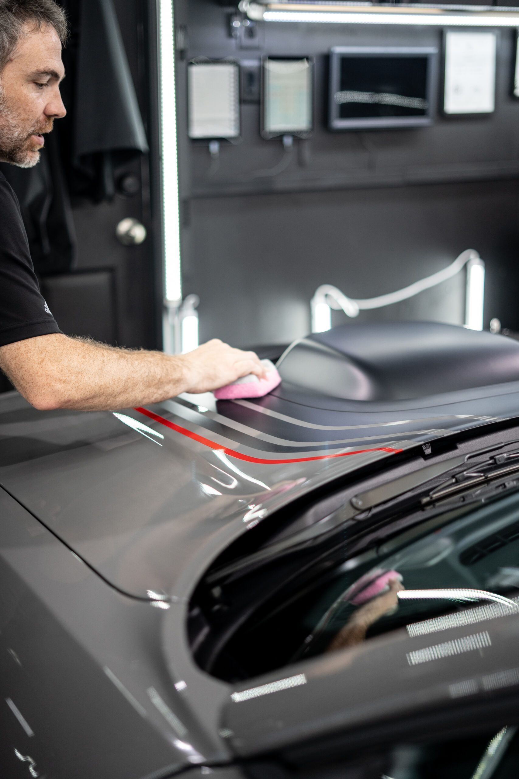 A man is cleaning the hood of a car in a garage.