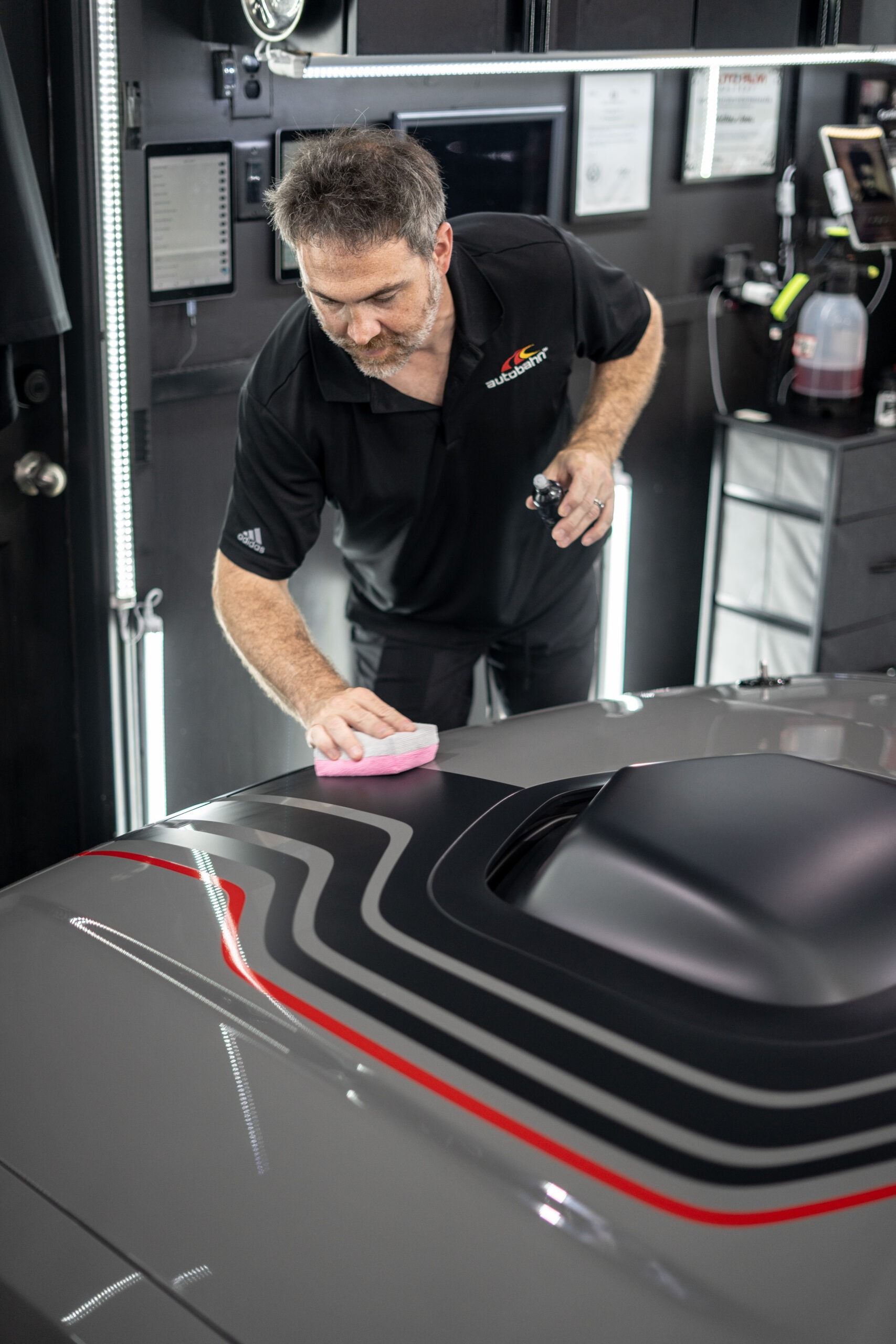 A man is cleaning the hood of a car in a garage.
