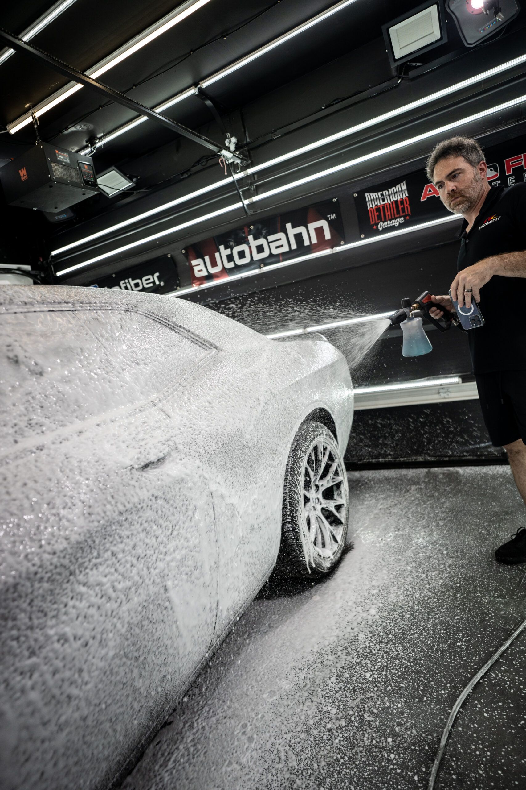 A man is washing a car with foam in a garage.