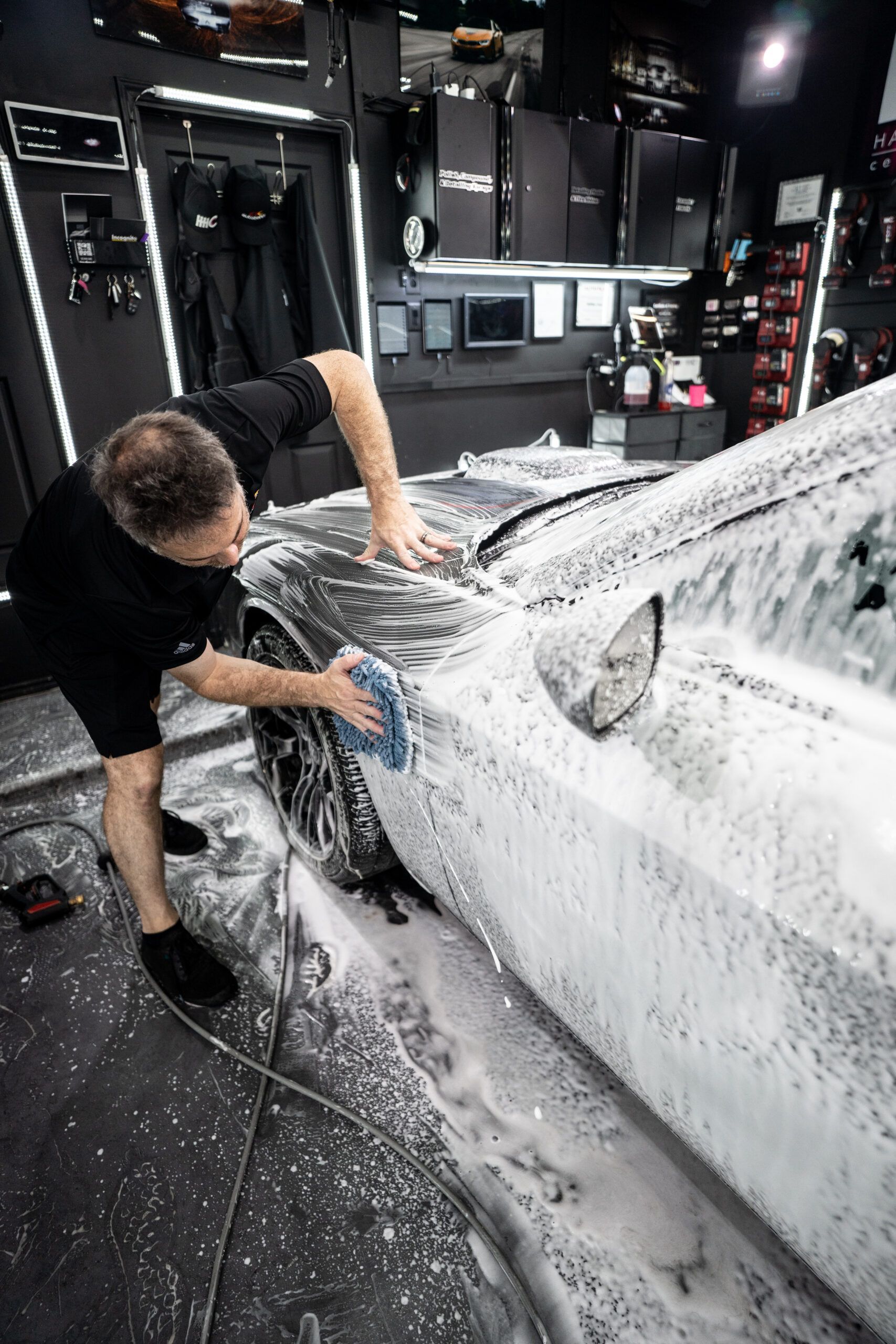 A man is washing a car with foam in a garage.