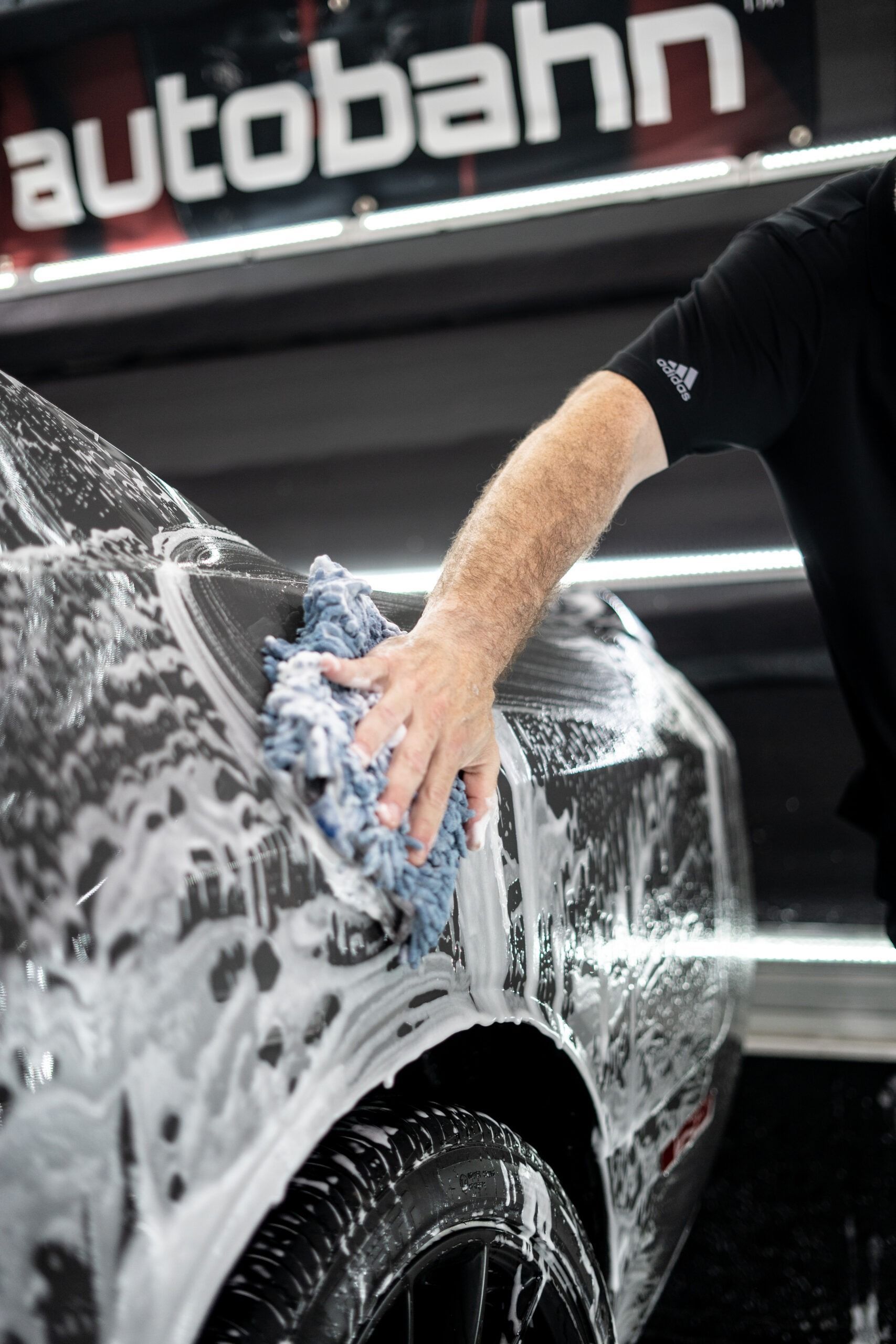 A man is washing a car with a cloth in front of an autobahn sign.