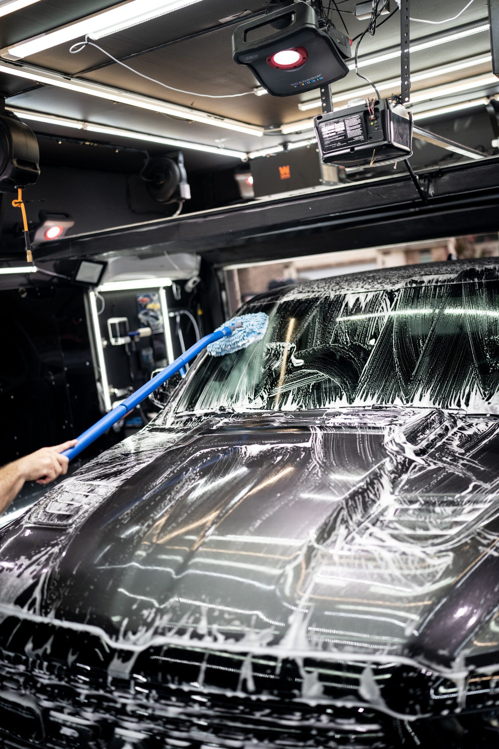 A person is washing a car with a brush in a garage.